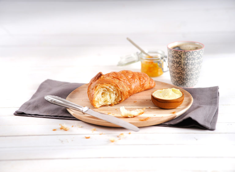 Croissant auf Holzbrett mit Butter und Marmelade