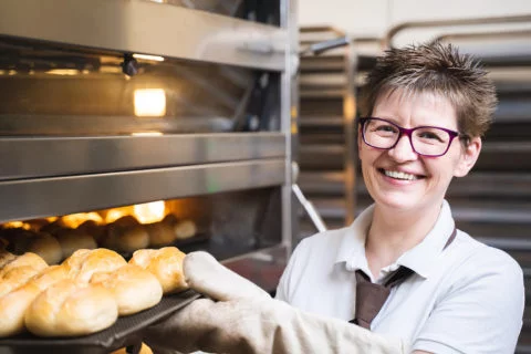 Verkäuferin vor Ofen beim Brötchenbacken